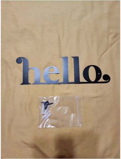 Black metal "hello" entry door sign with screws on tan fabric background.